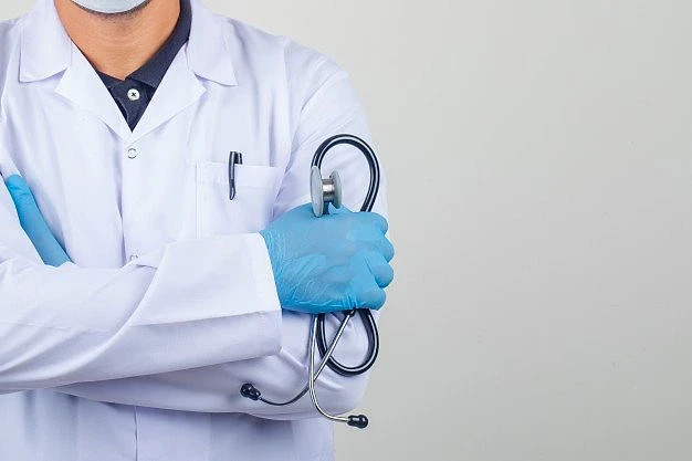 2026 doktor maaşları ve uzmanlık bilgileri Mavi eldiven giymiş bir doktor, kollarını kavuşturmuş ve stetoskop tutuyor.