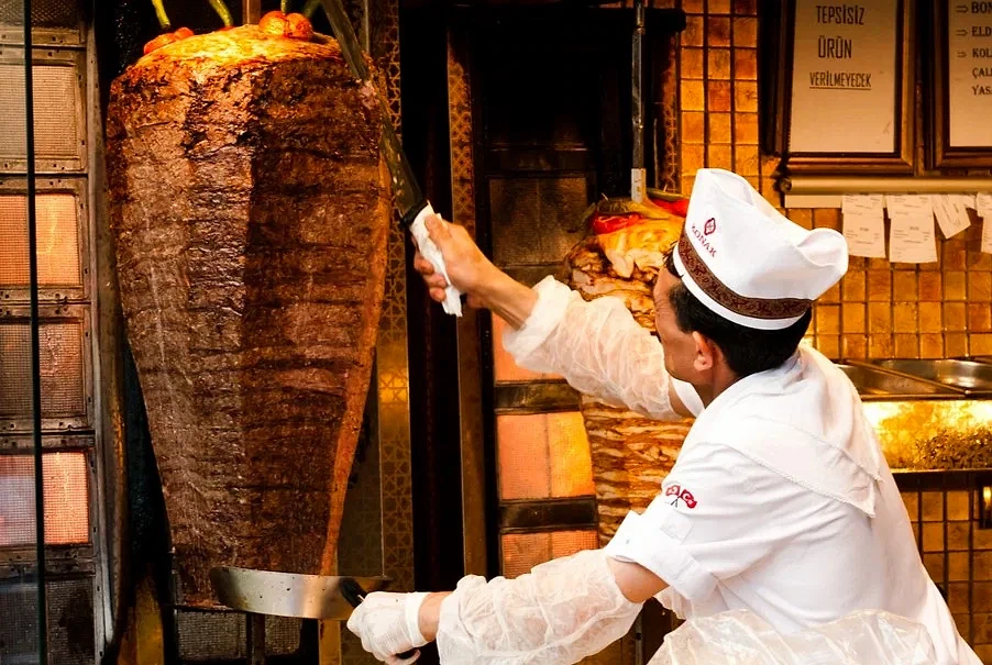 Dönerci mesleği ve çalışma şekli hakkında bilgi Döner kebap hazırlayan bir şef, döneri keserken dikkatle çalışıyor.