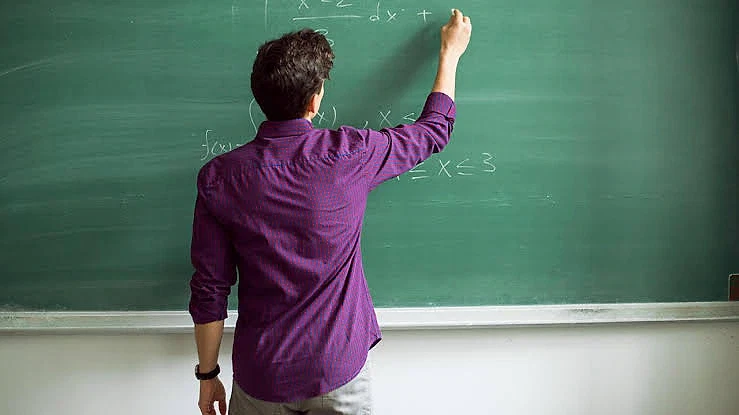 2026 öğretmen maaşları hakkında detaylı bilgi Siyah tahtada matematik formülleri yazan bir öğretmen, eğitim ortamı.