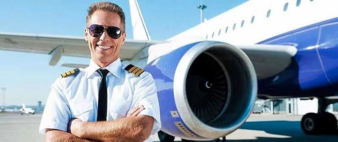 Pilotaj Bölümü ve Kariyer Fırsatları Pilotaj alanında uzman bir pilot, uçak motorunun önünde gülümseyerek poz veriyor.