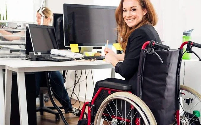 Engelli maaşları ve başvuru şartları hakkında bilgi Engelli bireyin ofiste çalıştığı, tekerlekli sandalyede oturduğu bir an.
