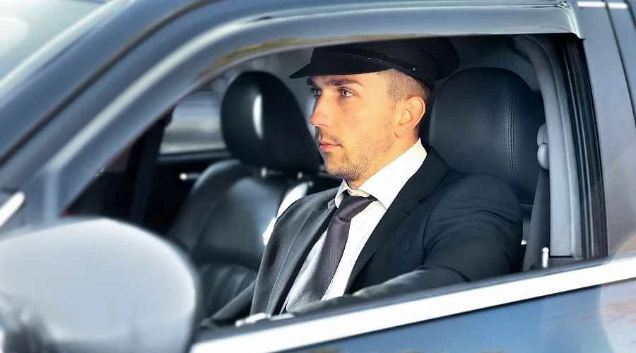 Lüks araçlarda profesyonel şoför hizmeti Şık giyimli bir şoför, lüks bir araçta direksiyon başında oturuyor.